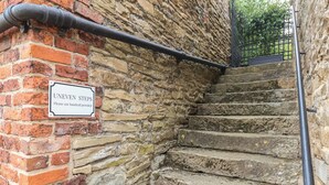 A stone staircase with a sign reading "UNEVEN STEPS" and a handrail. - The Annex at Manor Farm (York)