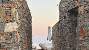 A narrow stone corridor with a lounge chair and umbrella, leading to a beach view. - Pentanemi Folegandros (Folegandros)