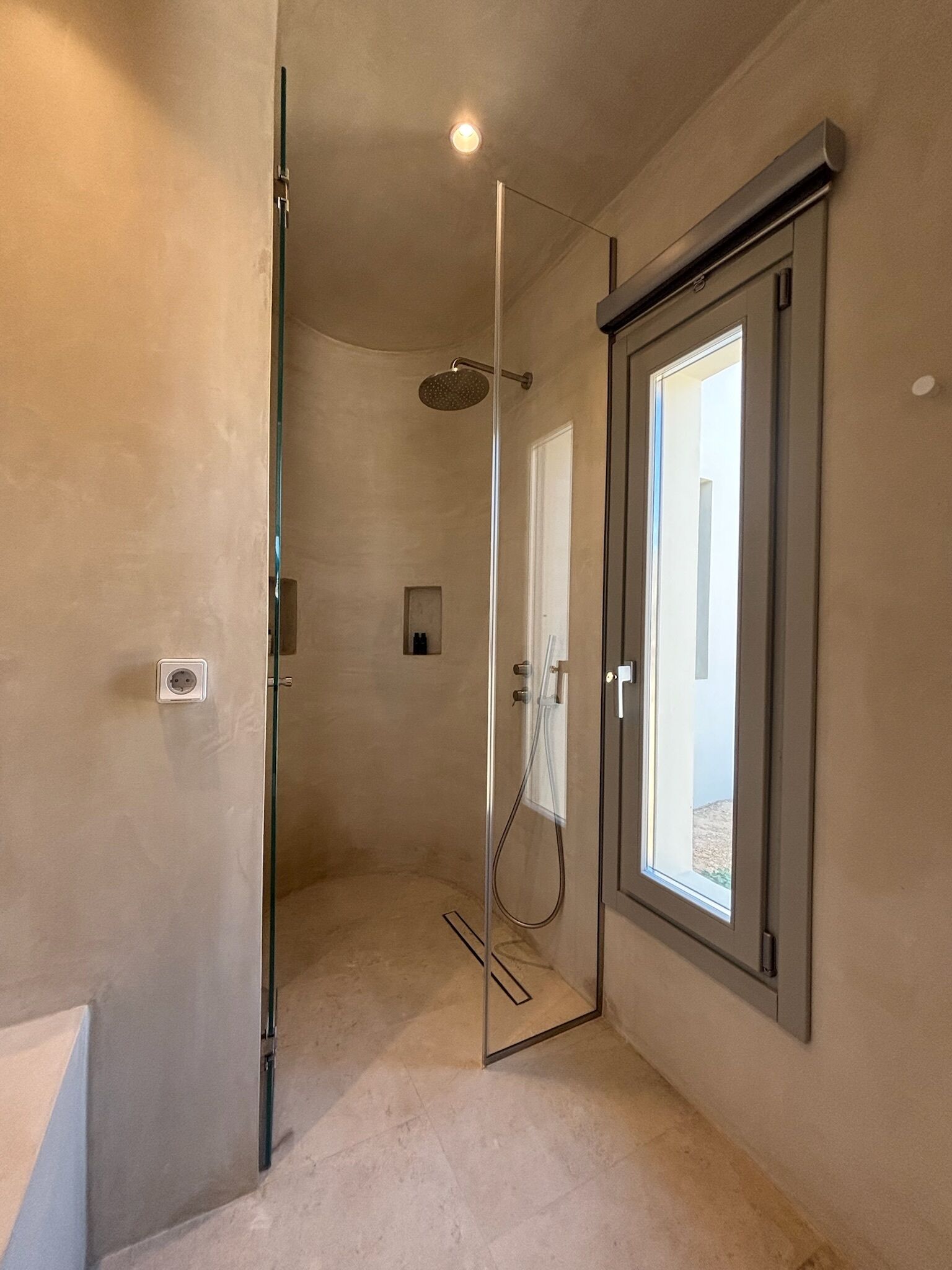 Un baño moderno con cabina de ducha de vidrio, un enchufe visible y una puerta que da a un espacio exterior.