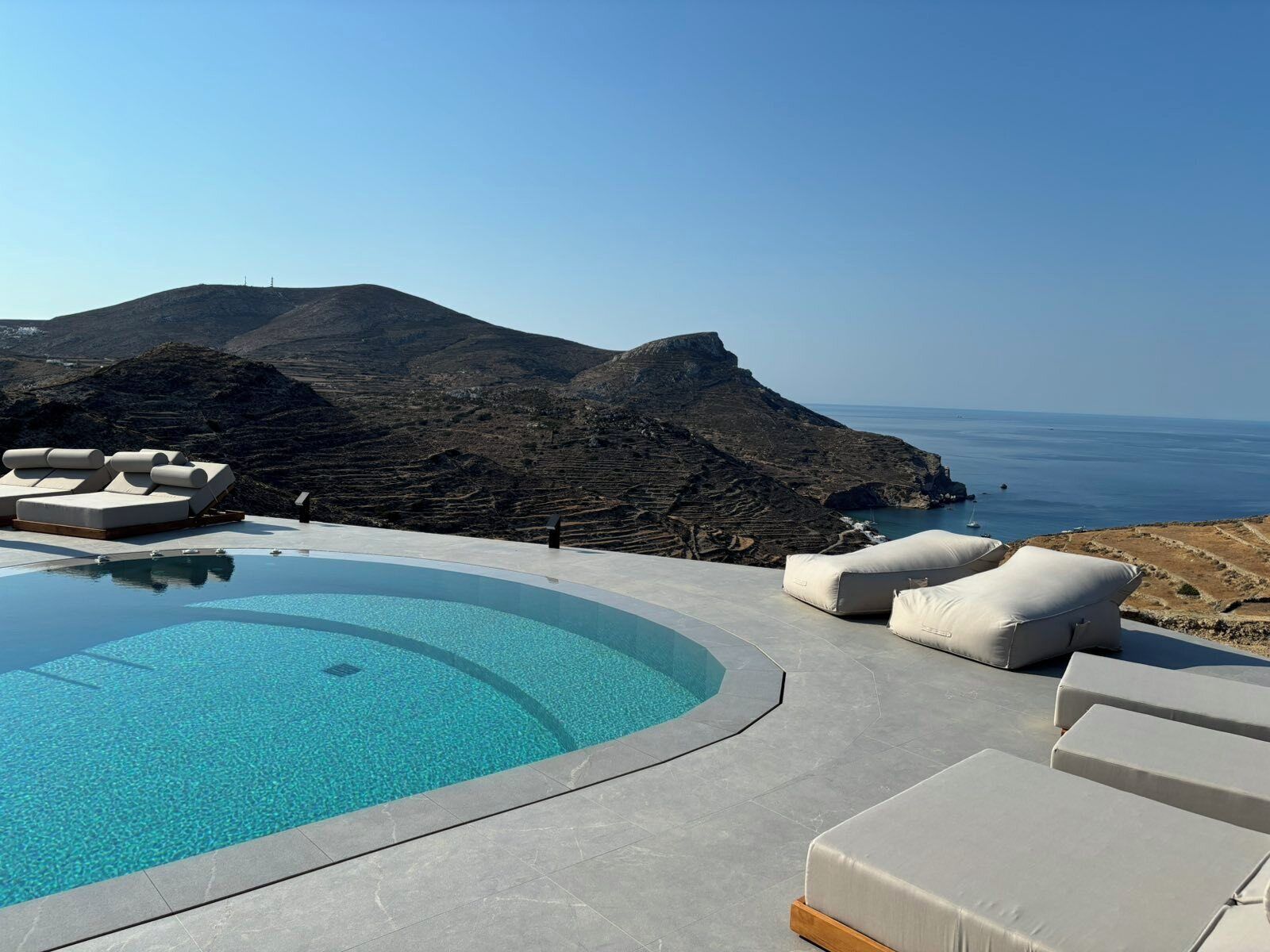 Una piscina con sillones de descanso y vistas al mar y a las montañas.
