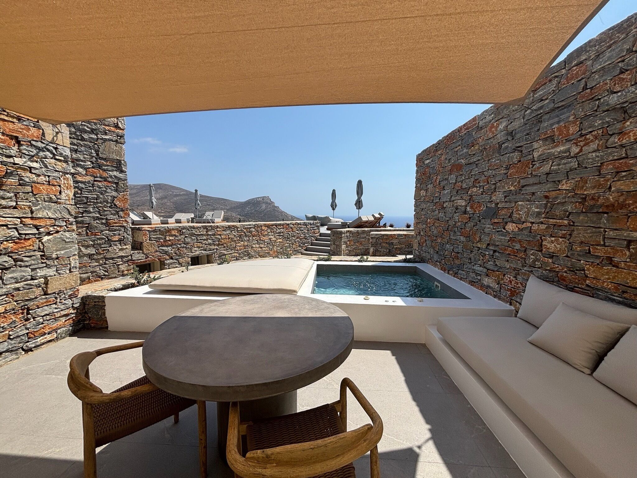 Espaço ao ar livre com paredes de pedra, piscina, mesa e sofá.