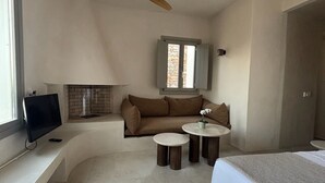A modern bedroom with a bed, a TV on a built-in shelf, a ceiling fan, a stone wall, and a window. - Pentanemi Folegandros (Folegandros)