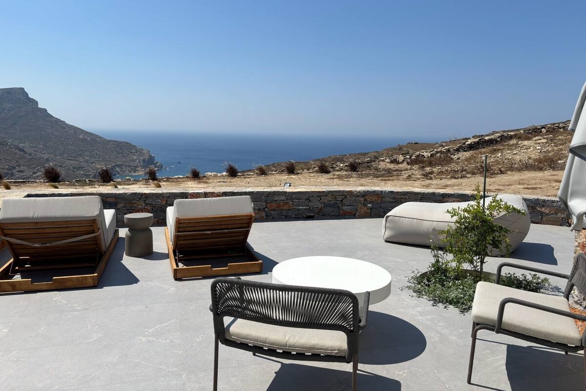 Eine Terrasse mit Sitzgelegenheiten, eine Steinmauer und Blick auf das Meer und die Berge.