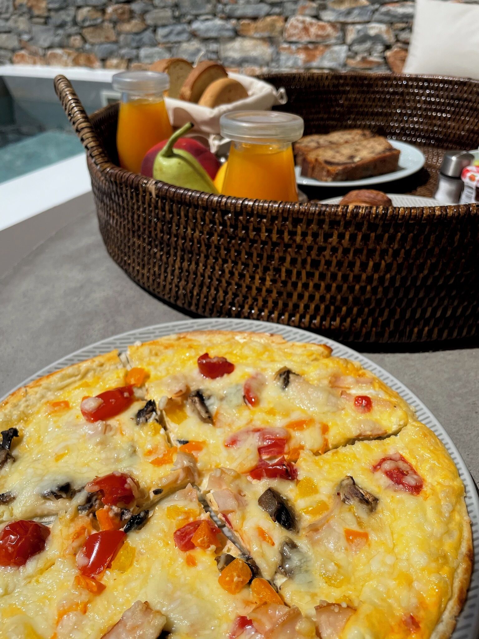 A breakfast setting with a plate of omelette, a wicker basket with bread and fruit, and a glass of orange juice.