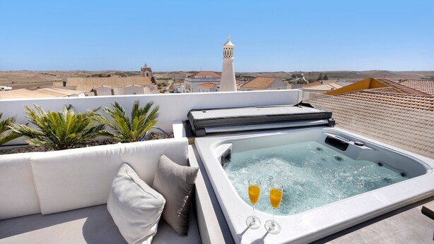 Een terras op het dak met een jacuzzi, buitenmeubels en uitzicht op het landschap.