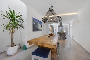 A modern kitchen with a wooden table, a potted plant, and a hanging light fixture.