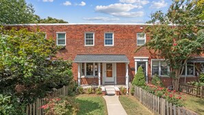 A two-story brick house with a front porch, a small front yard, and a wooden fence.