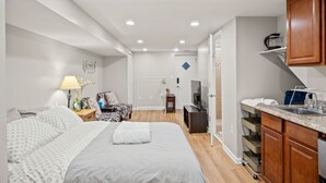 A modern hotel room with a large bed, a desk, a TV, and a kitchenette.