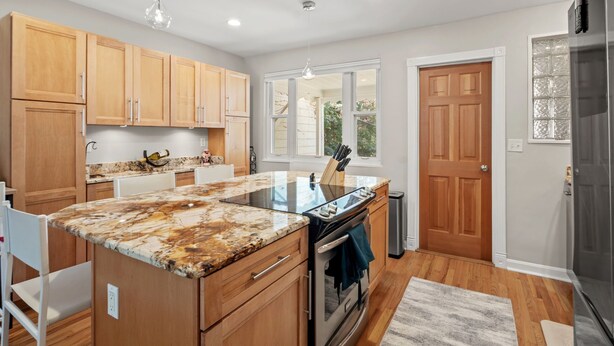 A modern kitchen with wooden cabinets, a granite countertop, stainless steel appliances, and a large window providing natural light.