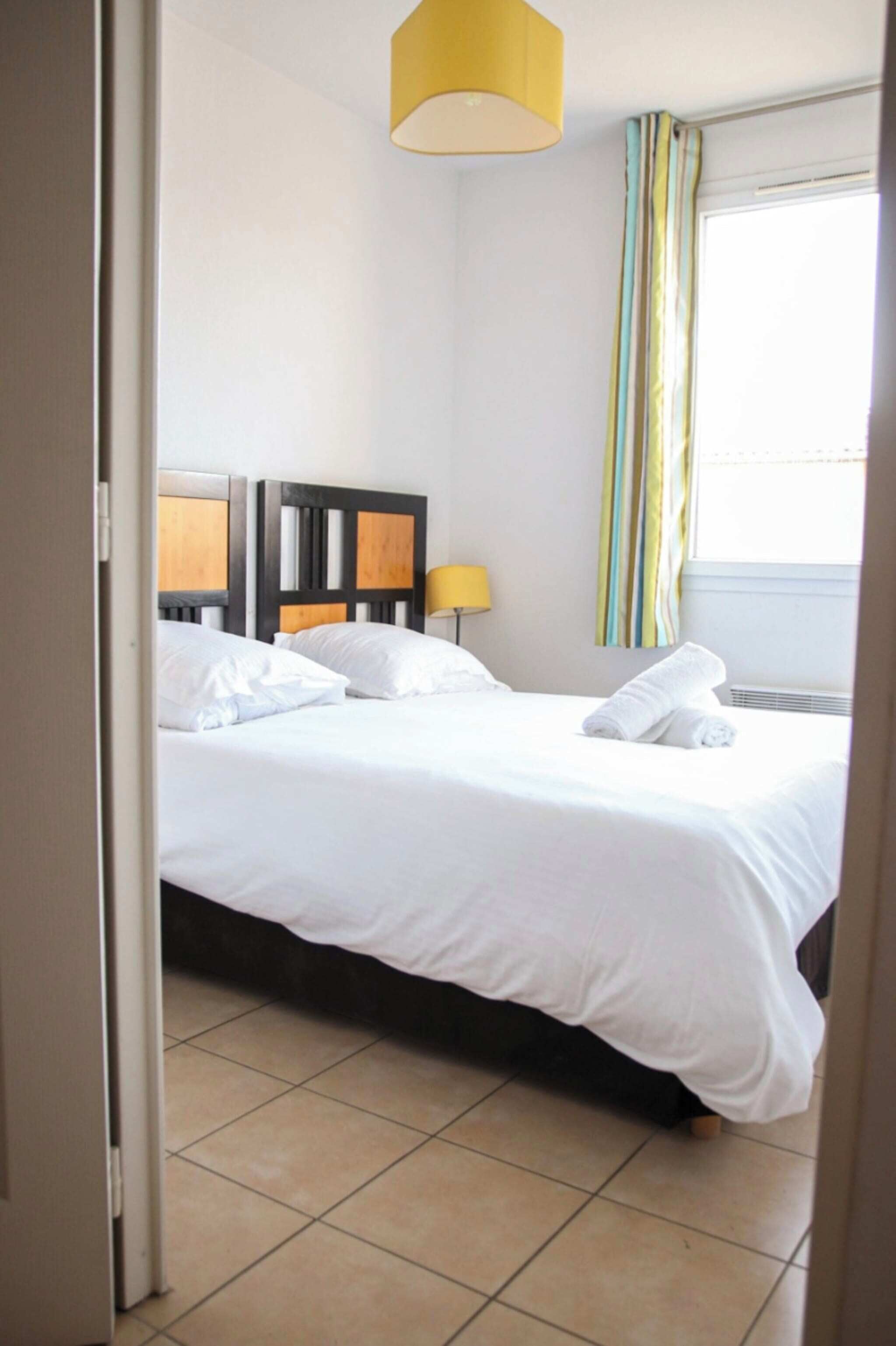 A hotel room with a bed, a nightstand, a lamp, and a window with curtains.