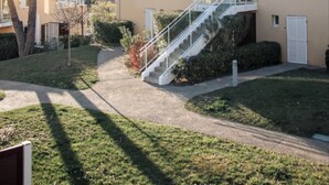 Un edificio residencial con una escalera que lleva a un balcón, rodeado de un césped cuidado y árboles.