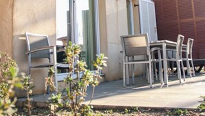 Un patio exterior con una mesa, sillas, una puerta corrediza de vidrio y un pequeño jardín.