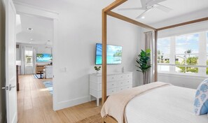 A bedroom with a bed, a TV, a dresser, and a window with a view.