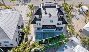 A multi-story building with a rooftop terrace, a swimming pool, and a beachside location.