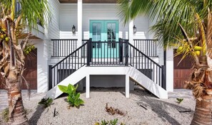 Un bâtiment à deux étages doté d’un balcon, de palmiers et d’une porte turquoise.