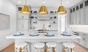 A modern kitchen with a central island, pendant lighting, and bar stools. - Beautiful Beach house! Heated pool and spa! (Holmes Beach)