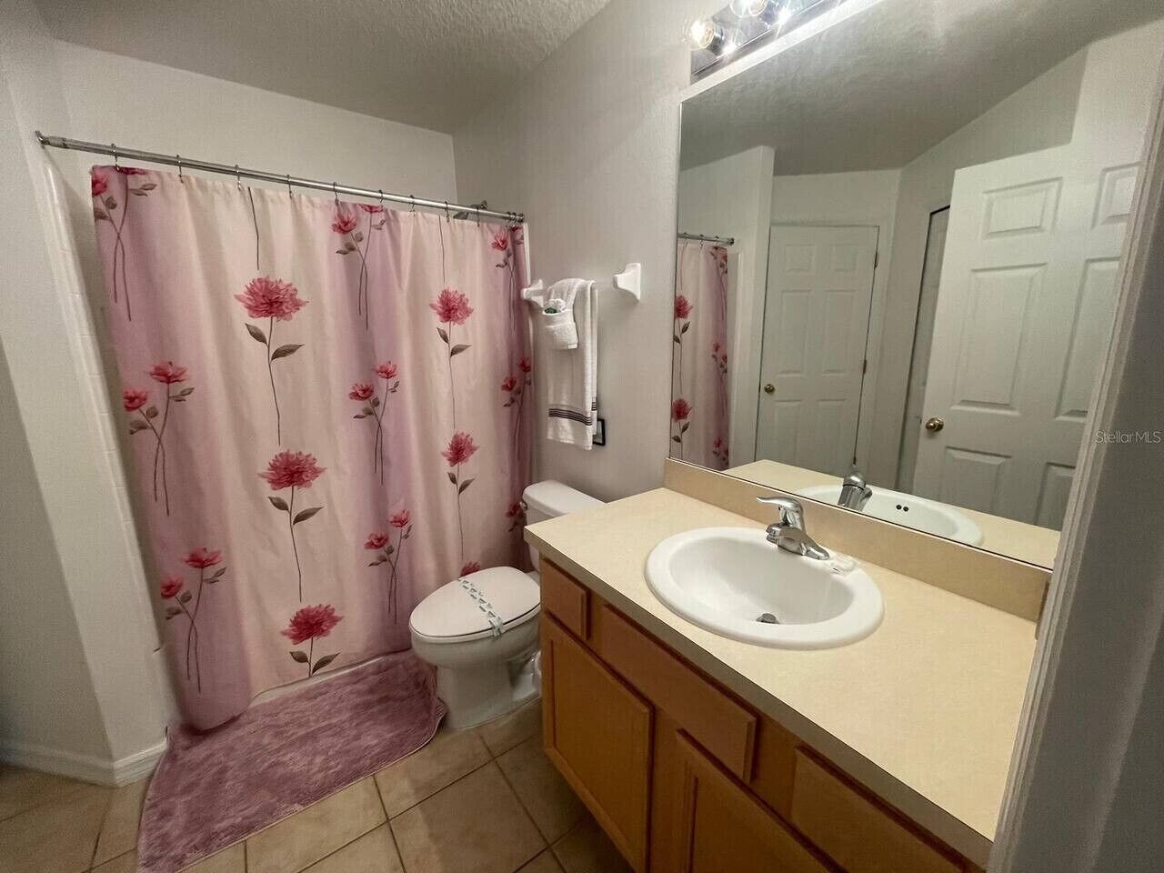 Une salle de bain équipée de toilettes, d’un lavabo, d’un miroir et d’un rideau de douche à motifs floraux.