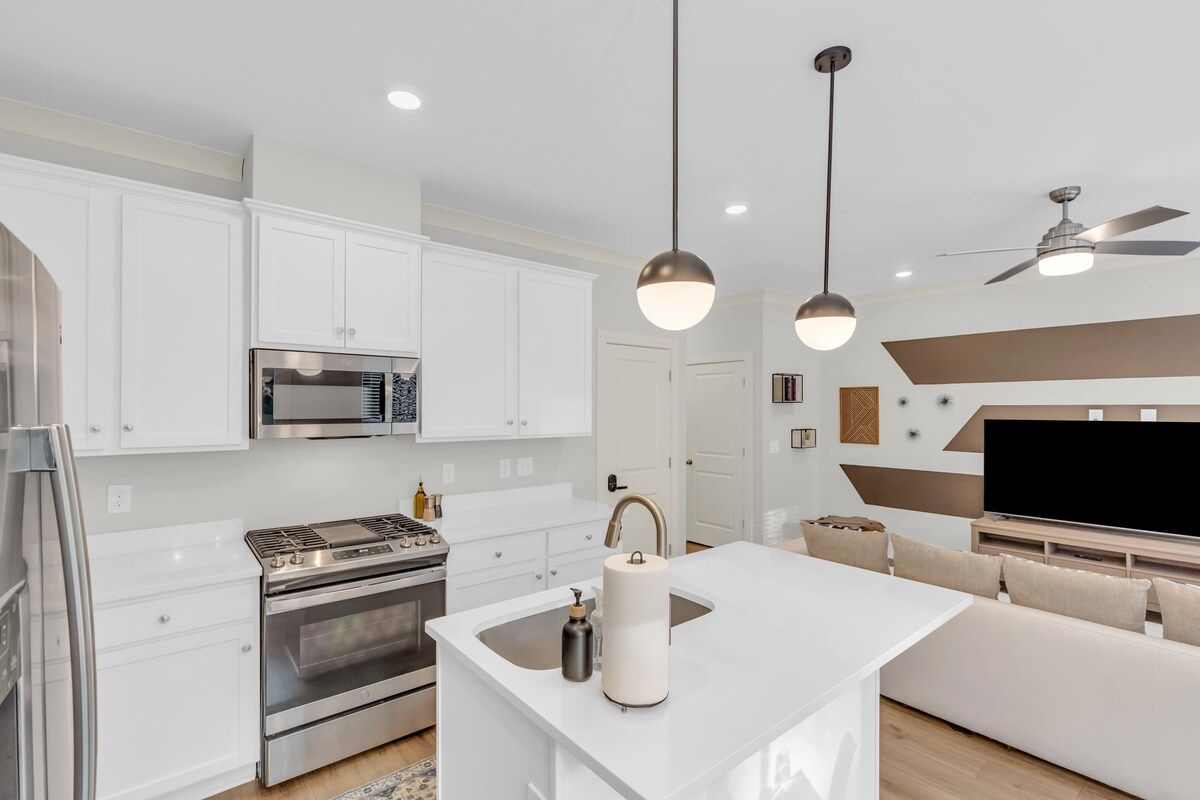 A modern kitchen with white cabinetry, stainless steel appliances, and pendant lighting.