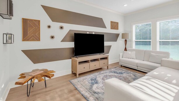 Ein modernes Wohnzimmer mit Flachbildfernseher, einem weißen Sofa und einem gemusterten Teppich.