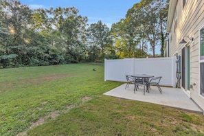 Ein Garten mit einer Terrassenfläche, einem Tisch und Stühlen.