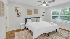 Ein Schlafzimmer mit einem Bett, einem Deckenventilator, einem Fenster mit Jalousien und Wandbildern.