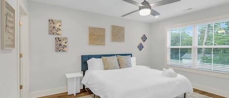 Une chambre à coucher avec un lit, un ventilateur de plafond, une fenêtre avec des stores et des œuvres d’art murales.