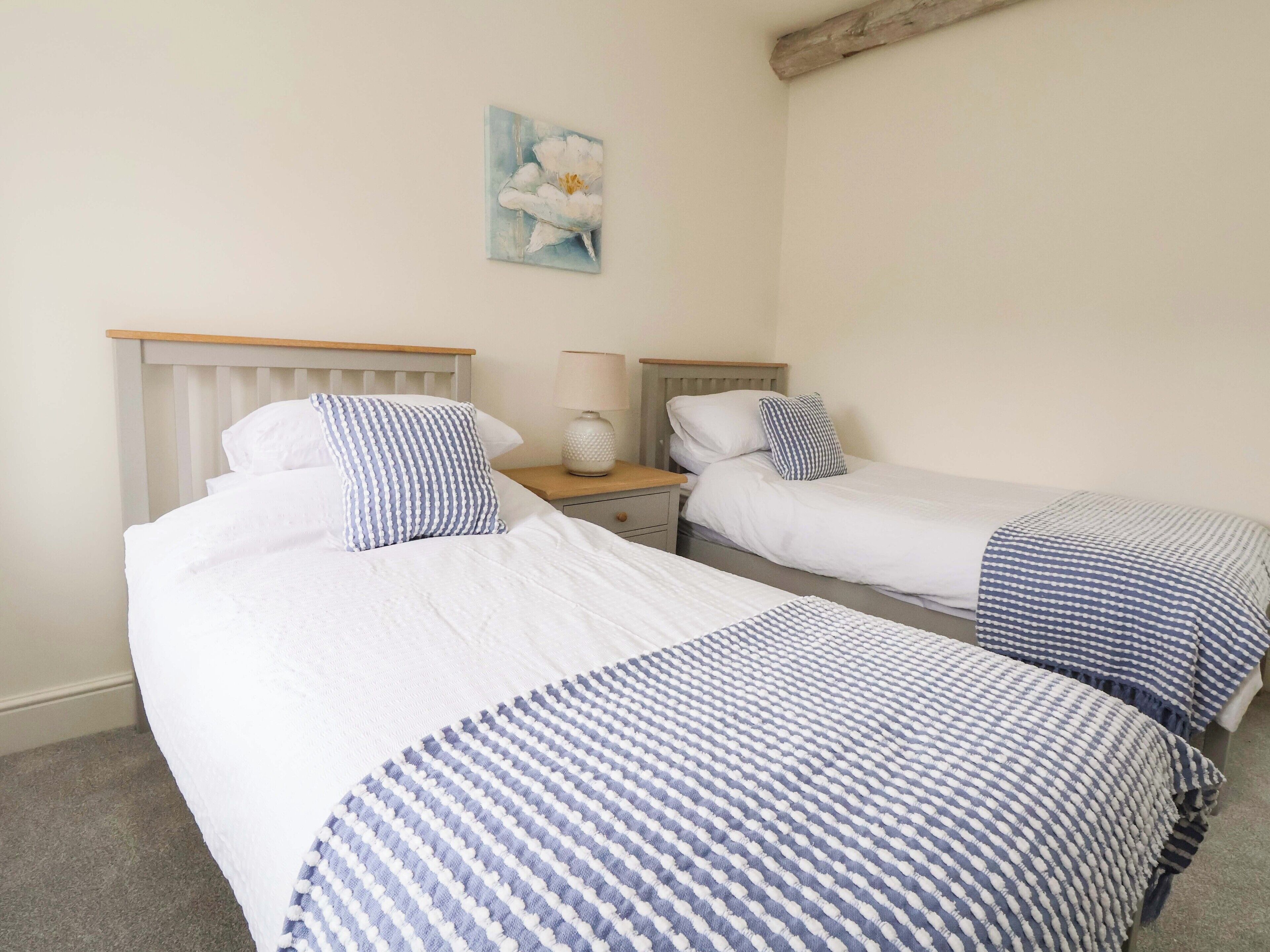Une chambre à coucher avec deux lits, chacun recouvert d’une couvre-lit à rayures blanches et bleues, doté d’une tête de lit en bois et agrémenté d’une table de chevet avec une lampe.