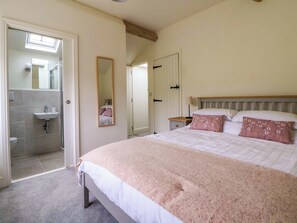 Un dormitorio con cama, mesita de noche, espejo y baño visible a través de una puerta abierta.