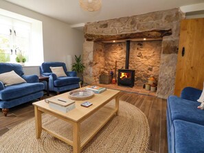 A cozy living room with a stone fireplace, blue sofas, and a wooden coffee table. - Isfryn (Mold)
