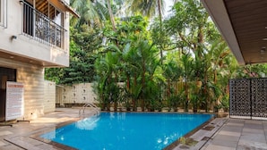 A swimming pool surrounded by lush greenery, with a poolside area and a sign indicating pool rules. - MERITAS GRAND INN (Calangute)