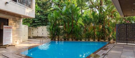 A swimming pool surrounded by lush greenery, with a poolside area and a sign indicating pool rules.