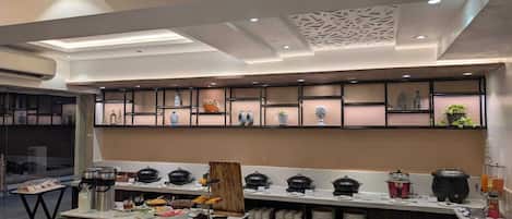 A modern kitchen with a central island, built-in shelves with decorative items, and a variety of food and drink dispensers.