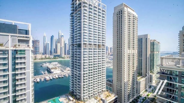 Un edificio de gran altura con un diseño arquitectónico moderno, rodeado de otros edificios altos y una marina con barcos.