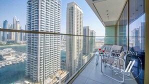 Un edificio alto con balcón que tiene barandilla de vidrio, una mesa con sillas y vistas a la ciudad y al agua.