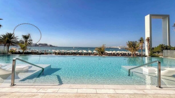 Une piscine à l’eau d’un bleu cristallin, une grande roue en arrière-plan et une vue sur la mer.