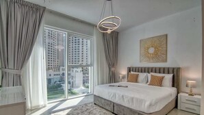 Une chambre moderne avec un grand lit, une vue sur les immeubles à travers une porte coulissante et un luminaire au plafond.