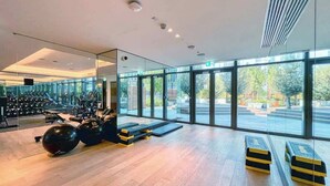 Un gimnasio moderno con piso de madera, equipo de ejercicio y amplias ventanas con vistas al exterior.
