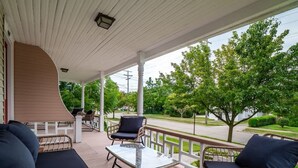 A covered porch with wicker furniture, a glass table, and a view of a residential street. - Historic District - Fully Stocked Kitchen-Sleeps 6 (Bedford)