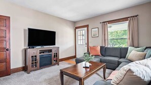 A living room with a flat-screen TV, wooden entertainment unit, grey sofa, and a coffee table. - Historic District - Fully Stocked Kitchen-Sleeps 6 (Bedford)