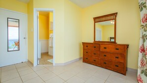 Quarto com cômoda de madeira, um espelho e uma porta que dá para outro espaço.