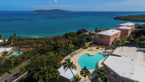 Um resort com piscina, palmeiras e vista para o oceano.