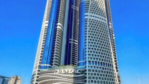Ein modernes Hochhaus mit einer geschwungenen Fassade und einem gut sichtbaren 'DAMAC'-Schild am Fuße des Gebäudes.