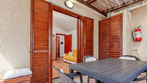 A room with a wooden table and chairs, a sofa, and a fire extinguisher mounted on the wall. - Raggio di sole Olbia (Olbia)