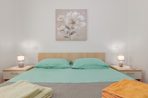 Un dormitorio con una cama, dos mesitas de noche, dos lámparas, un cuadro en la pared y una ventana.