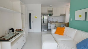 A modern kitchen with white cabinets, a stainless steel refrigerator, and a dining area with a white table and chairs. - COBAR0117 - Edifício Yacht Residencial (Salvador)