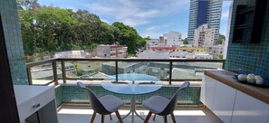 Un balcón con una mesa de vidrio y dos sillas, con vistas a un paisaje urbano de edificios y árboles.