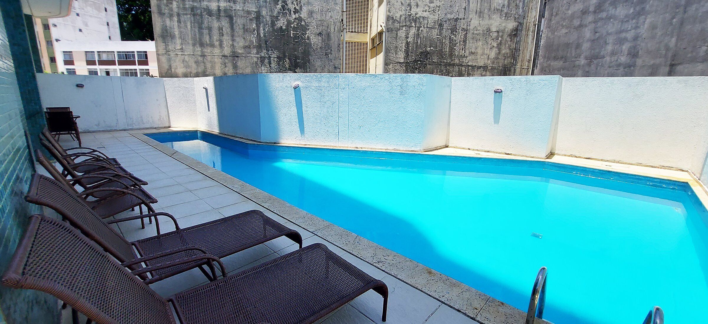 A swimming pool with a tiled deck and metal chairs.