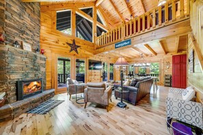 A spacious wooden interior with a stone fireplace, leather sofas, and a balcony.