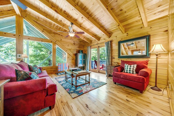 A wooden cabin interior with a red sofa, a wooden coffee table, and a ceiling fan.