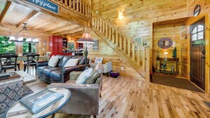 Un interior de cabaña acogedor, con una escalera, paredes de madera, un sofá de cuero y una zona de comedor.